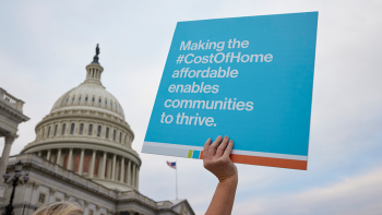 Hand holding sign that says "Making the Cost of Home affordable enables communities to thrive" with U.S. Capitol building in background