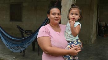 Mujer sostiene en brazos a una niña pequeña frente a su vivienda, que cuenta con piso de concreto y un entorno más seguro y adecuado para la vida cotidiana. La imagen refleja el impacto de una mejora habitacional en el bienestar de las familias. 