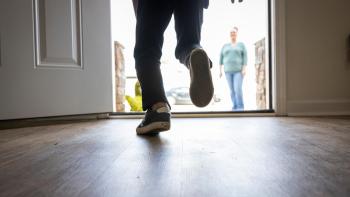 A child's feet are seen running past an open front door toward his mother who is waiting on the front lawn.