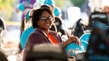 Smiling woman holding a blue Habitat hard hat with stickers on it.
