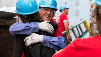 A Midland County HFH board member and DuPont volunteer, both wearing blue hard hats, greet each other on the jobsite.