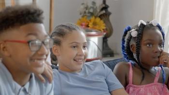 Three kids sitting on a couch in their living room. 