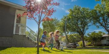 Three children playing soccer in front yard of Habitat home.