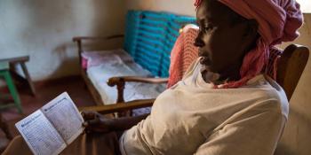 a woman from Kenya sitting on a chair holding an open book with her microloan payments