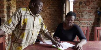 a woman from Uganda sitting at the table. She is studying her microloan payments book.