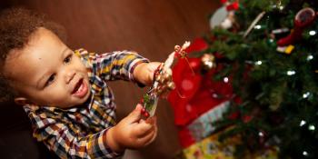Little boy hangs ornament on Christmas tree.