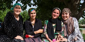 Photo: four women holding roses sitting on a bench under the tree