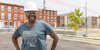 Woman in a hardhat standing in front of a brick building.