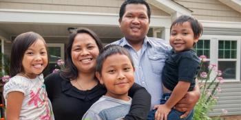 family of five smiling in front of house. 