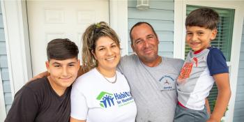 Parents with two sons smiling in front of house. 