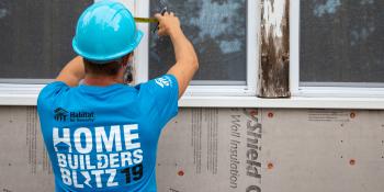 Volunteer wearing a shirt that says "Home Builders Blitz 2019" works on a window on a build site.