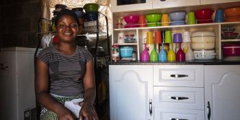 Photo: Lucy in her kitchen. Colorful dishes tidied up in the cupboard behind her.