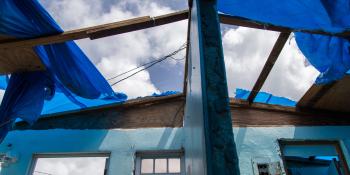 View from inside a hurricane-damaged Puerto Rico house of blue tarps partially covering a missing roof with view of clouds.