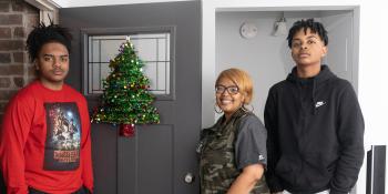 The family stands at their door thats decorated with a Christmas wreath.