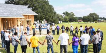 A circle of community members linking hands in a park.