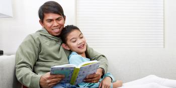 A little girl and her father reading on a couch together. 