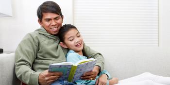 A little girl and her father reading on a couch together.