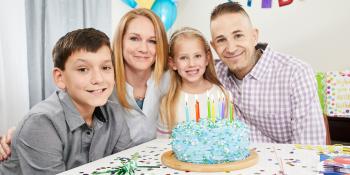 Mother, father, brother and sister celebrate son’s birthday with a cake and party at home.  