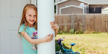 Young girl with red hair smiles and hugs a column in front of her Habitat house.