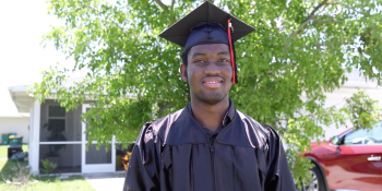 young man in graduation cap and gown smiling in front of his Habitat home.
