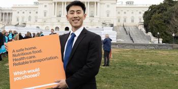 Man holding sign in Washington, D.C. that says "A safe home. Nutritious food. Health care. Reliable transportation. Which would you choose?"