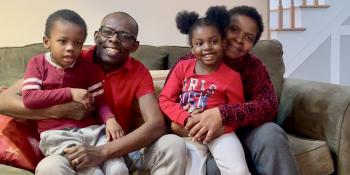 Ingrid, her husband, and their children smiling on their couch in their Habitat home.