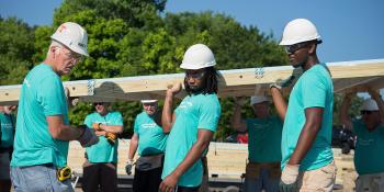 A group of Thrivent volunteers in blue T-shirts and white hard hats on a build site.