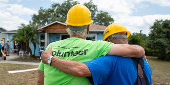 Shot from behind of two Habitat volunteers in hardhats with their arms around one another