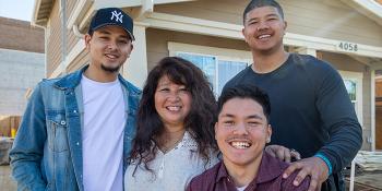 Mother with three sons smiling in front of their home.