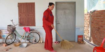 Cambodian homeowner Sophal sweeping the floor outside her home