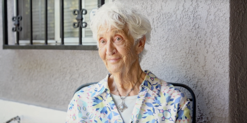 Older adult Rachel sits in front of her home.