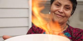 Maria holds up a bowl that contains a fire burning her final mortgage payment.