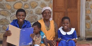 A woman and three children sit outside their home smiling