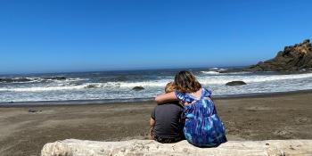 Photo of brother and sister sitting on driftwood log looking out at the ocean