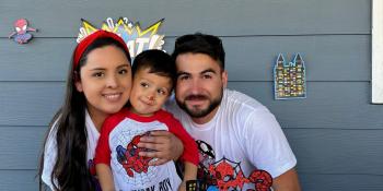 Mother, son and father posing in front of spiderman birthday decorations.