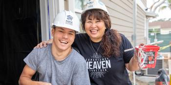 Young man and his mom smile together while painting on a Habitat build site.