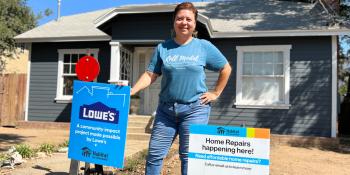 Woman standing in front of her home with signs saying home repairs are happening here thanks to Habitat and Lowe's