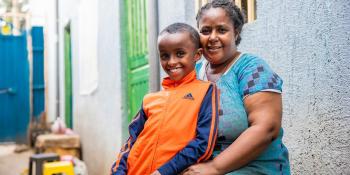 A woman and her son sit outside their home smiling