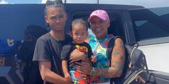 A mother poses smiling with her adolescent son and infant son. 