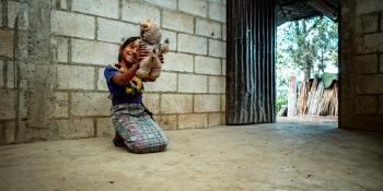 Little girl playing with doll while kneeling on a concrete floor