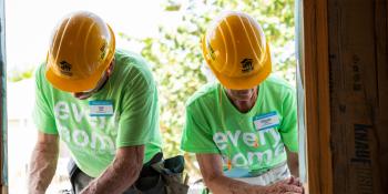 Two volunteers in hardhats work side by side on a Habitat build site