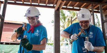 Two Global Village volunteers hammering a piece of wood during construction in Cambodia.