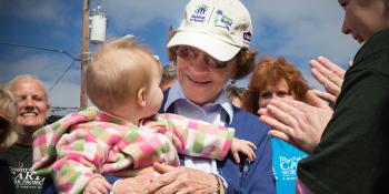 Mrs. Rosalynn Carter holding a baby, smiling a crowd of volunteers.