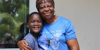 An older woman hugs her grandson outside her home.