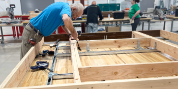 Man in blue shirt works on building a pre-fab wall panel inside a warehouse.