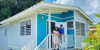 Homeowner Ishmael and his mother stand on the porch of their blue house.