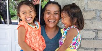 Mother holding two young daughters in front of a door.