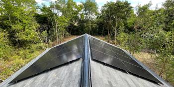 Solar panels on a roof with a lush green forest in the background.