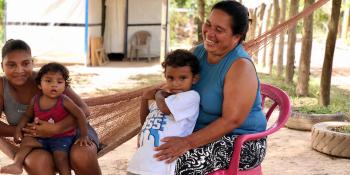 A mother sitting outside her home in Honduras, holding her child and smiling.