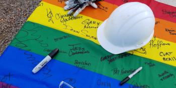 Photo of a signed rainbow flag with a white hard helmet on top.